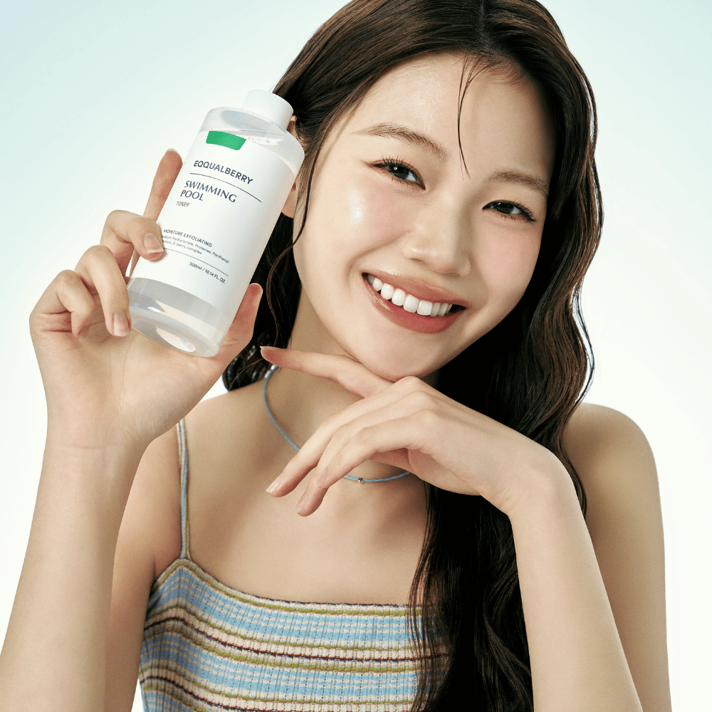 Mulher sorridente com pele radiante segurando Equalberry Swimming Pool Toner. Aparência fresca e natural com maquiagem leve e um visual de verão em tons azuis.