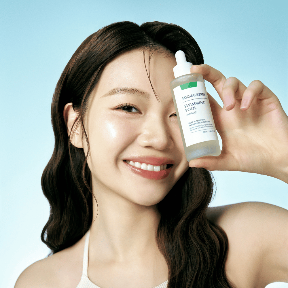 Uma mulher sorridente segura Eqqualberry Swimming Pool Ampoule, um produto de cuidados com a pele para hidratação intensa, em frente a um fundo azul claro.