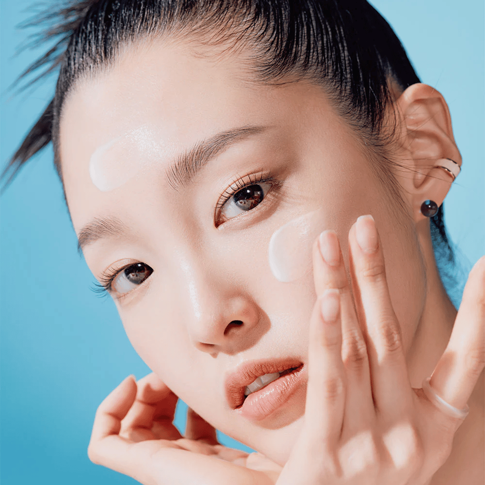 Uma mulher posa com as mãos no rosto em uma TOCOBO Bio Watery Sun Cream SPF50+ PA++++ campanha de cuidados naturais com a pele de 50ml.