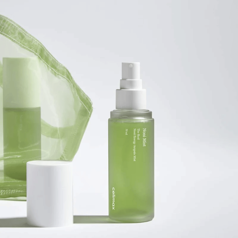 Uma garrafa com Celimax Noni Mist, um frasco spray verde com bomba branca, que está ao lado de uma tampa. O produto é embalado em um saco plástico transparente e é comercializado como Noni Energy Ampule Mist.