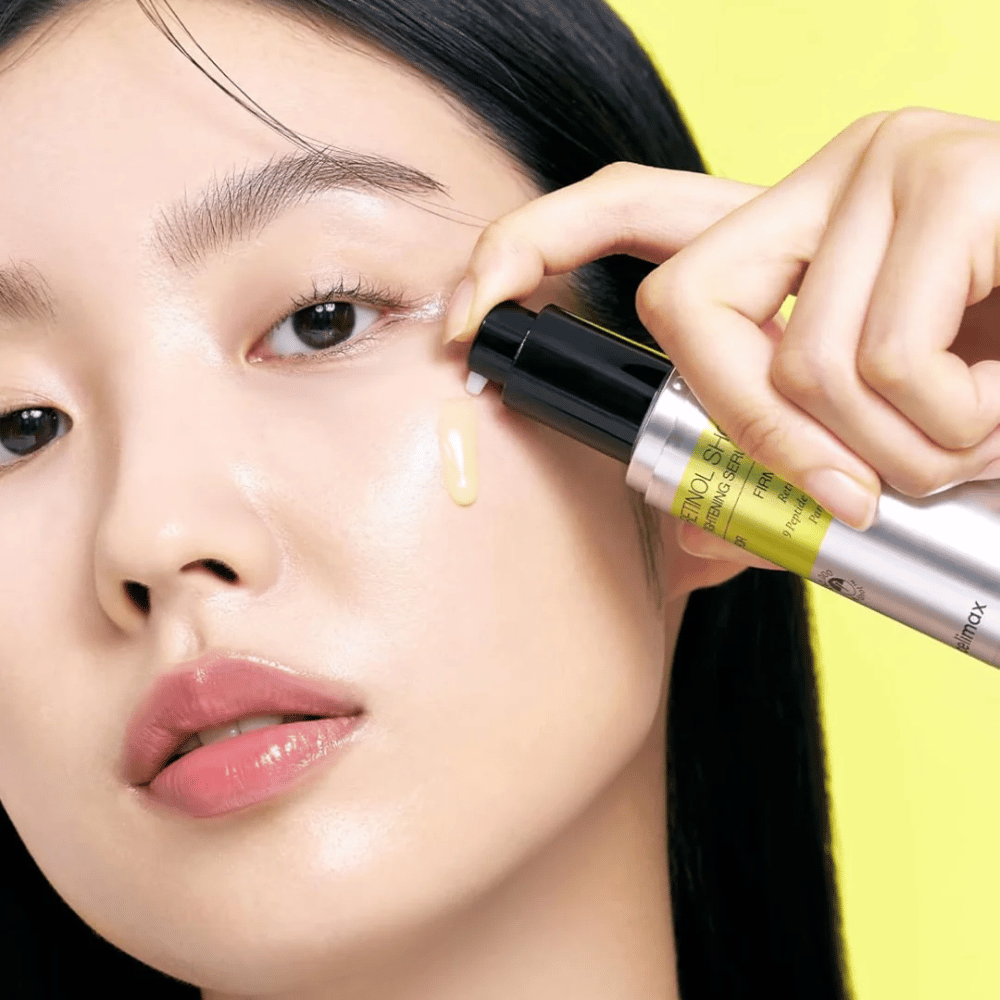 Modelo aplica The Vita-A Retinol Shot Tightening Serum de Tiam perto da área dos olhos, com foco no brilho da pele e na consistência amarela do soro.