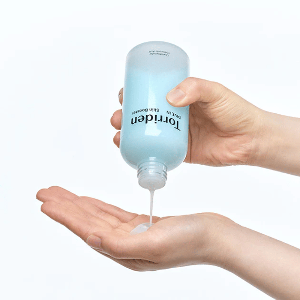 Mãos segurando uma garrafa de produto de cuidados com a pele e dispensando um líquido claro na palma da mão. A garrafa está etiquetada com "Torriden - DIVE-IN Low Molecule Hyaluronic Acid Skin Booster".