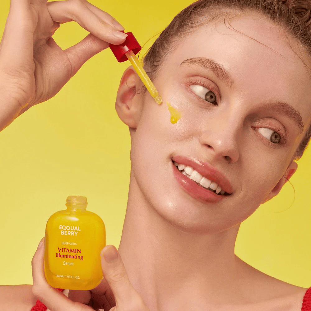 Mulher sorridente aplica Equal Berry Vitamin Illuminating Serum com uma pipeta. Pele fresca e radiante contra um fundo amarelo vibrante que combina com a cor do sérum.