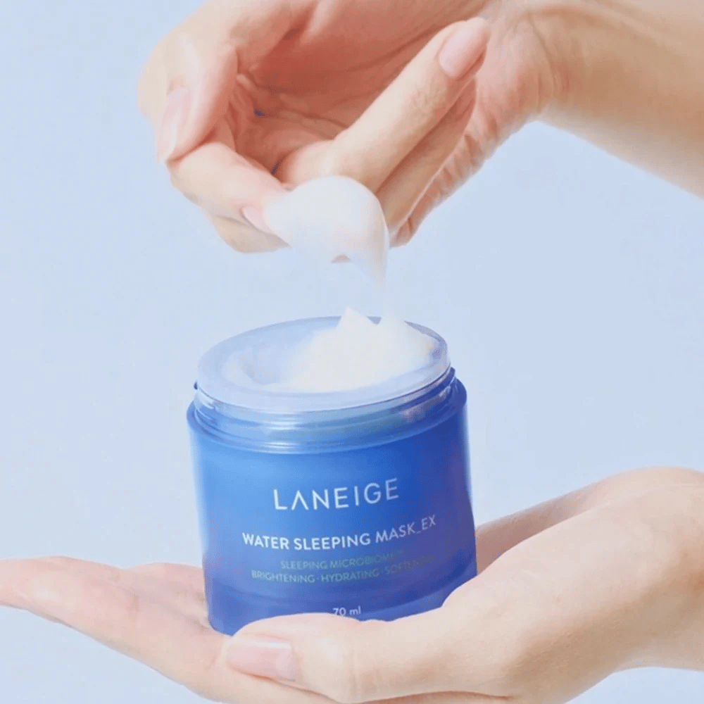 Uma mão colhe LANEIGE Water Sleeping Mask de um pote azul, com foco na consistência semelhante a gel contra um fundo azul claro.
