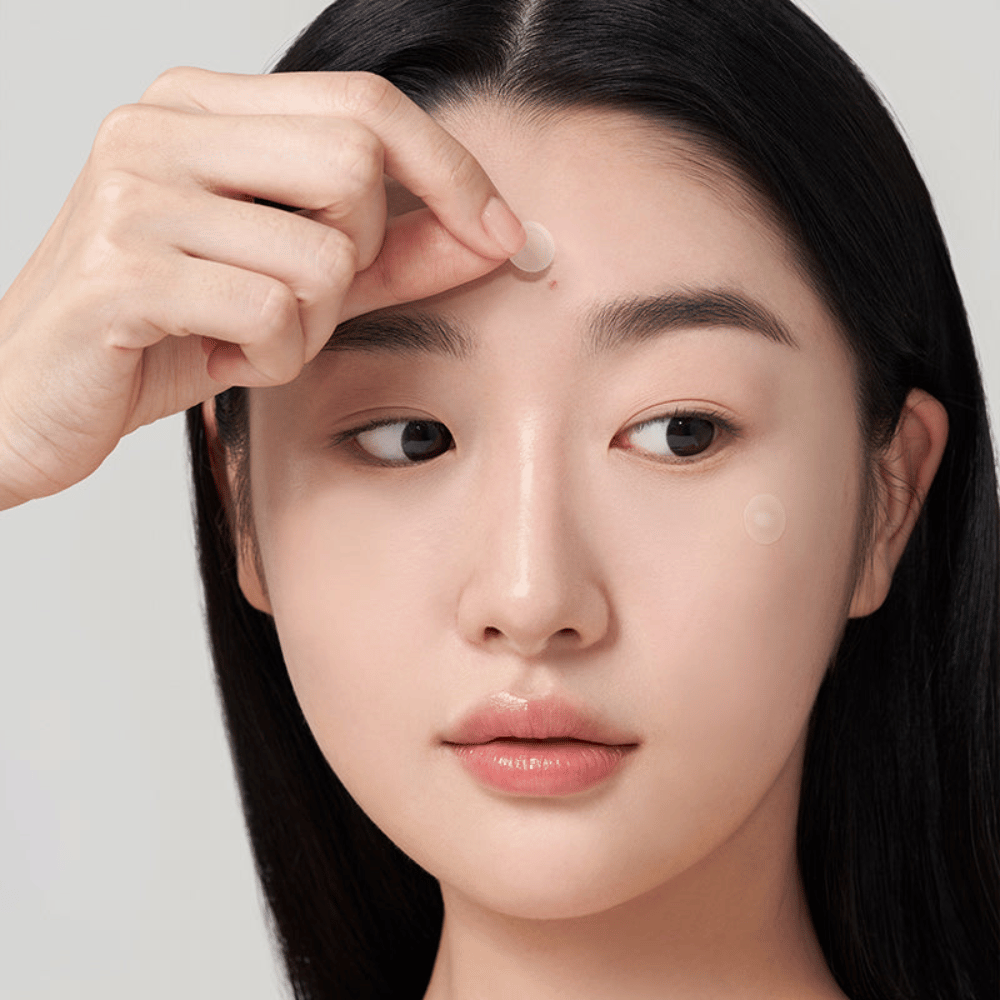 Pessoa aplica Purito Wonder Releaf Centella Spot Patch em espinha na testa, um adesivo discreto para acne que protege, acalma e apoia a cicatrização da pele.