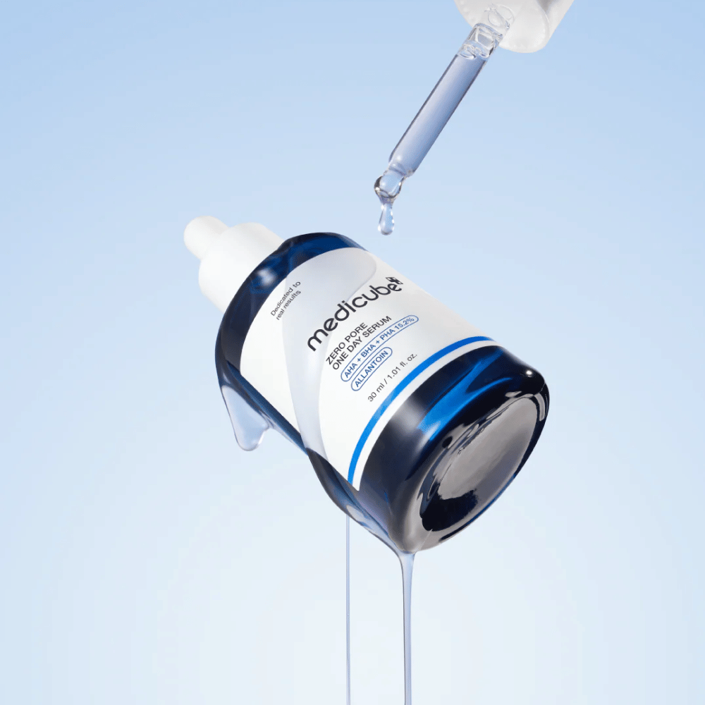 Garrafa de Medicube Zero Pore One Day Serum com conta-gotas e gotas de soro escorrendo sobre um fundo azul-claro.