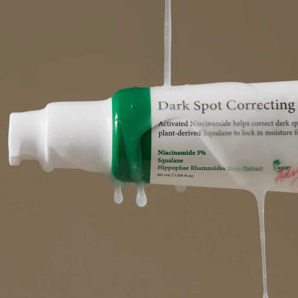 Close-up de um frasco de bomba de Axis-Y Dark Spot Correcting Glow Serum com embalagem branca e tampa verde, coberto por líquido transparente escorrendo.