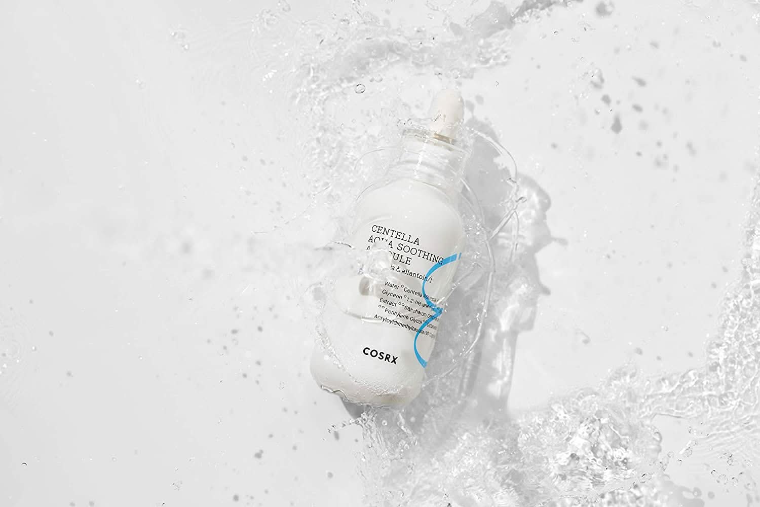 Uma garrafa COSRX Centella Aqua Soothing Ampoule 40ml que salpica sobre uma superfície branca, reduz vermelhidão e proporciona hidratação calmante.