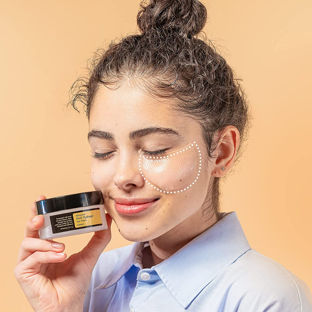 Uma mulher segurando um frasco COSRX Advanced Snail Hydrogel Eye Patch 60 unid de creme facial.