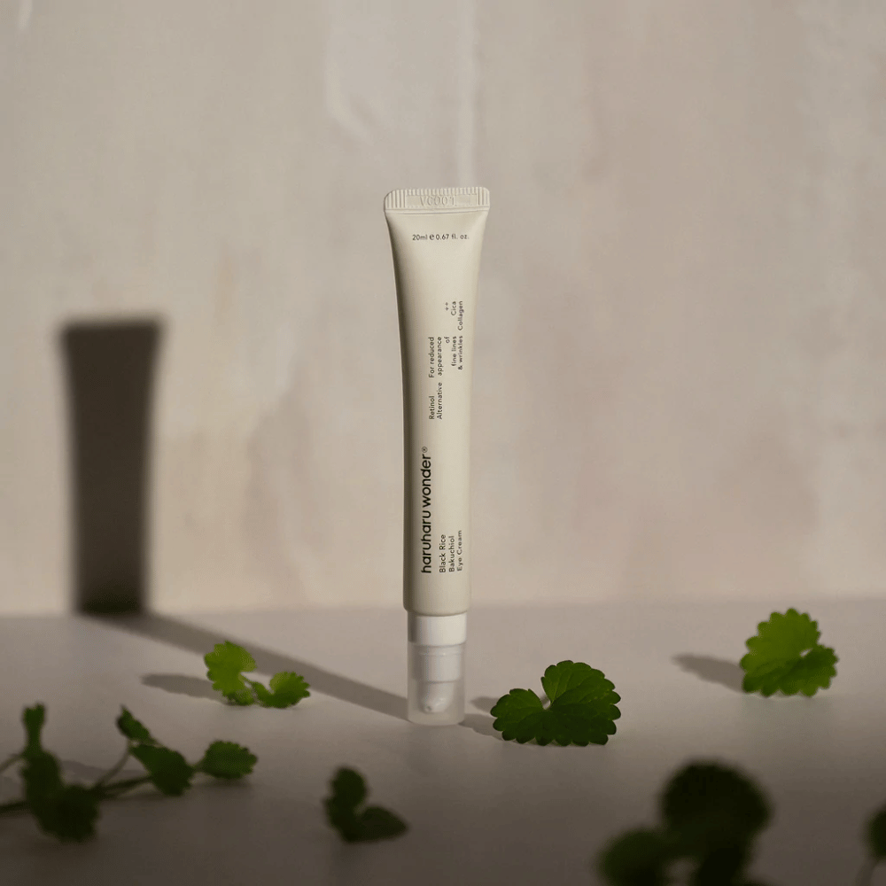 Um tubo Haruharu Wonder Black Rice Bakuchiol Eye Cream 20ml cercado por folhas verdes, focado na visibilidade de rugas e linhas finas.