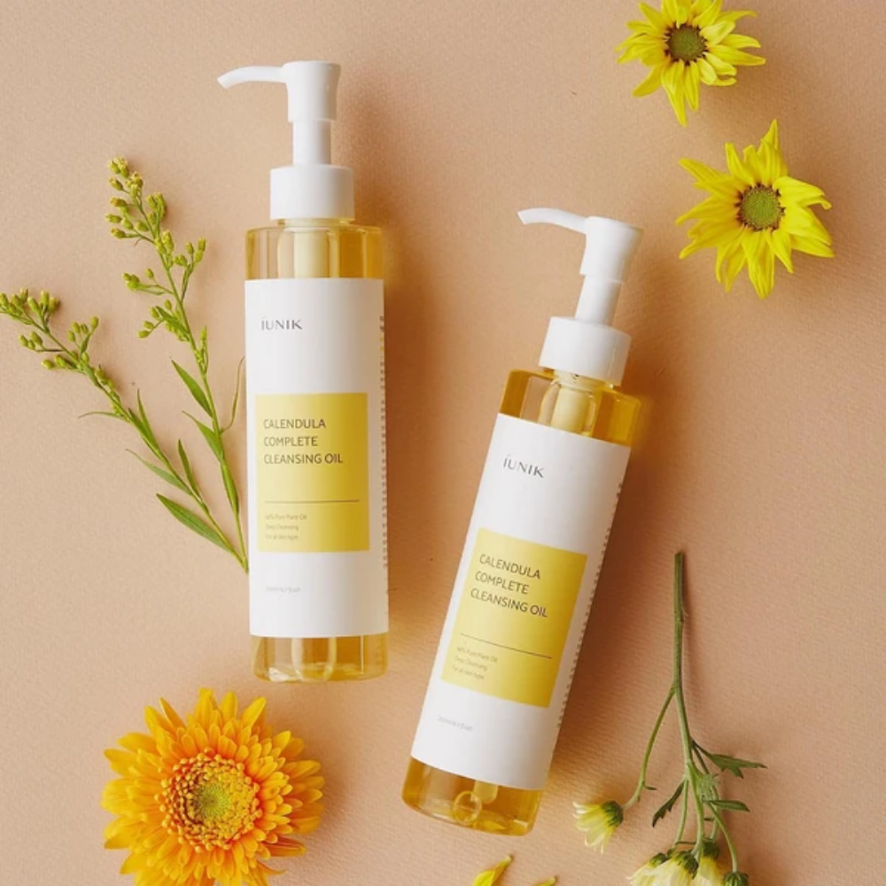 Duas garrafas iUNIK Calendula Complete Cleansing Oil 200ml com flores amarelas sobre fundo bege, infundidas com óleo vegetal.