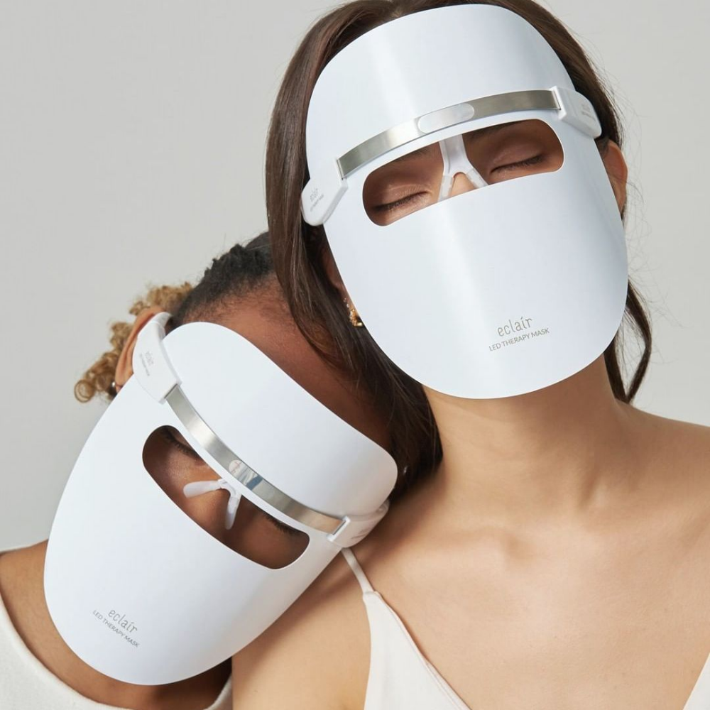 Duas mulheres usando máscaras brancas demonstram ECLAIR LED Therapy Mask para melhorias de tom de pele.