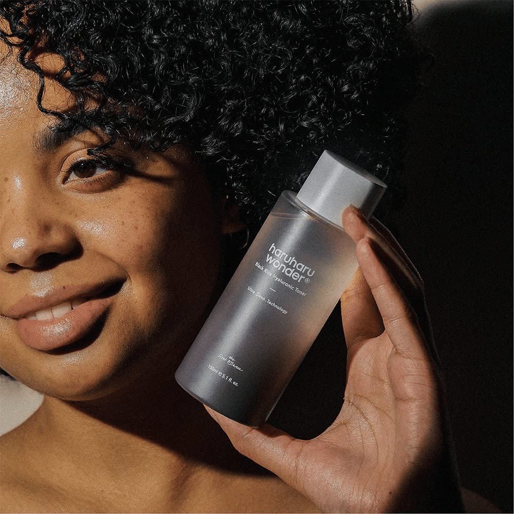 Uma mulher segurando uma garrafa de Haruharu Wonder Black Rice Hyaluronic Toner Original 150ml.